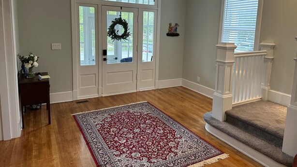 A spacious entryway with a large red and white patterned rug, a chandelier, and a staircase leading to an upper level. - Spacious restored 1914 historic home steps from the beach. (Cape Charles)