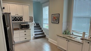 A kitchen with white cabinets, a stainless steel refrigerator, a microwave, and a staircase leading to a second floor. - Spacious restored 1914 historic home steps from the beach. (Cape Charles)