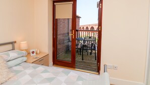 Ein Schlafzimmer mit Bett, Nachttisch, Lampe und einer Schiebetür zu einem Balkon mit Tisch und Stühlen.