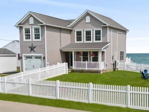 A two-story house with a white picket fence, a garage, and a front porch with a view of the ocean. - Hilton House on the Lake (Hilton)