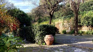Uma passagem de pedras em um jardim, com um vaso de terracota grande e folhagem densa.