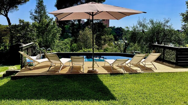 Uma área à beira da piscina com espreguiçadeiras e um grande guarda-sol.