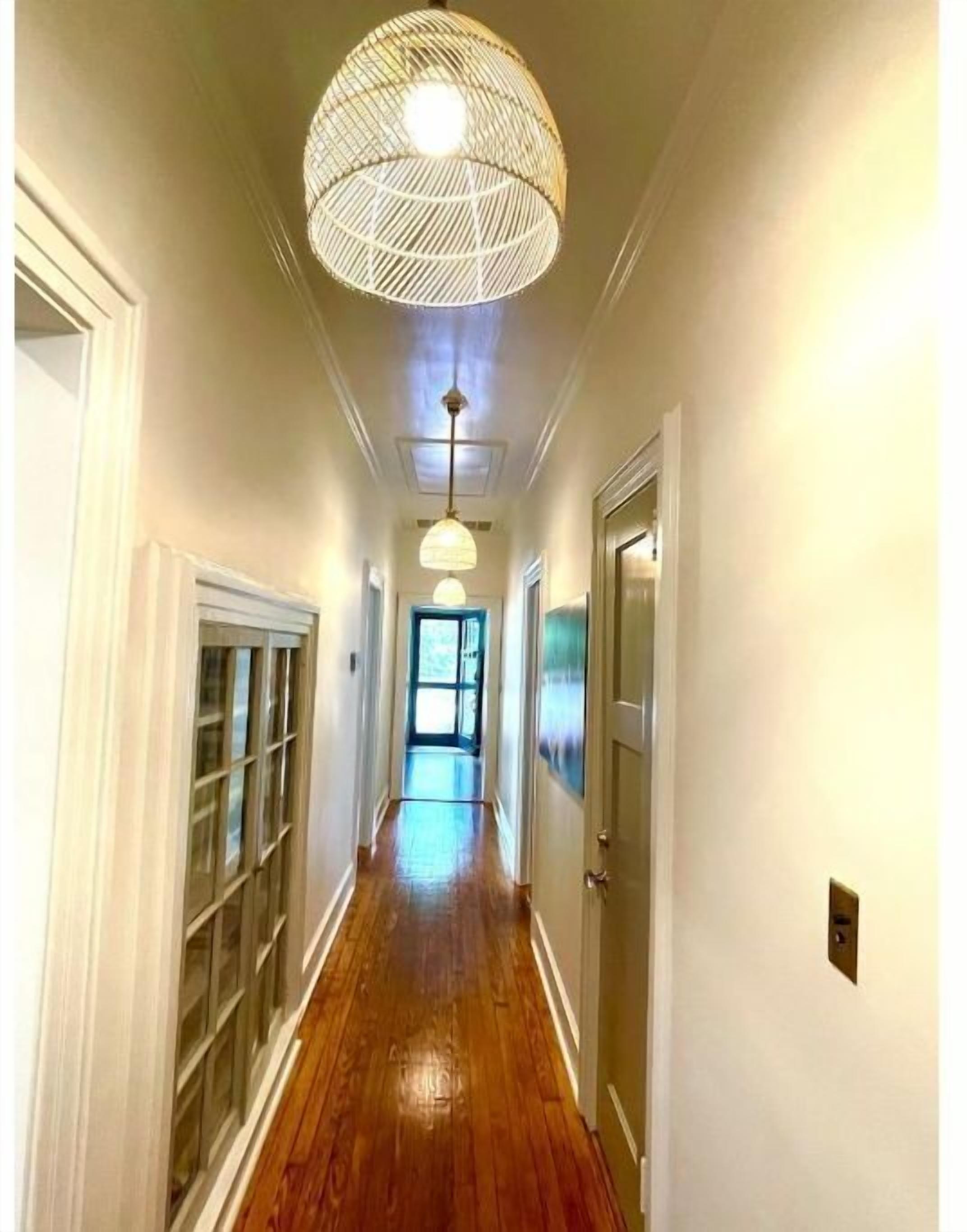 Un pasillo con piso de madera, paredes blancas y una lámpara en el techo.