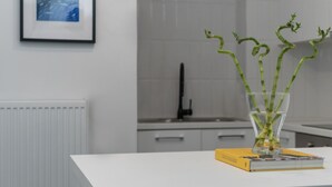 Una cocina moderna con encimera blanca, una silla negra y un florero con plantas verdes.