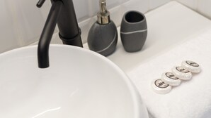 Un baño moderno con un lavamanos blanco, un grifo negro y un espejo encima. Hay dos jarrones grises y una toalla blanca en la encimera.