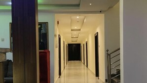 Un pasillo de hotel con suelo de mármol, un pilar de madera y una escalera a la derecha.