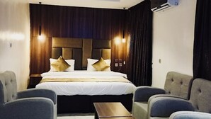 Una habitación de hotel moderna con una cama grande, dos sillones, una mesita y una lámpara de techo.