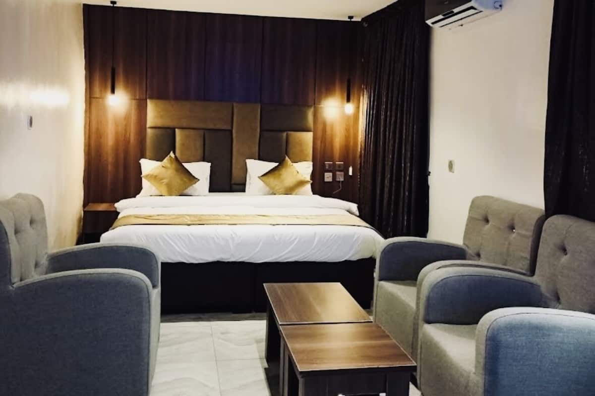 A modern hotel room with a large bed, two armchairs, a small table, and a ceiling light.