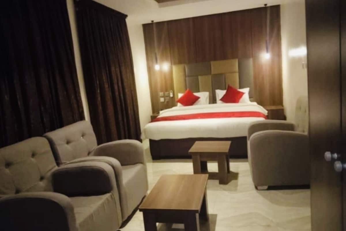 A hotel room with a large bed, two armchairs, a small table, and a curtain.