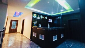 Un área de recepción con mostrador oscuro, una lámpara de neón y una televisión instalada en la pared.