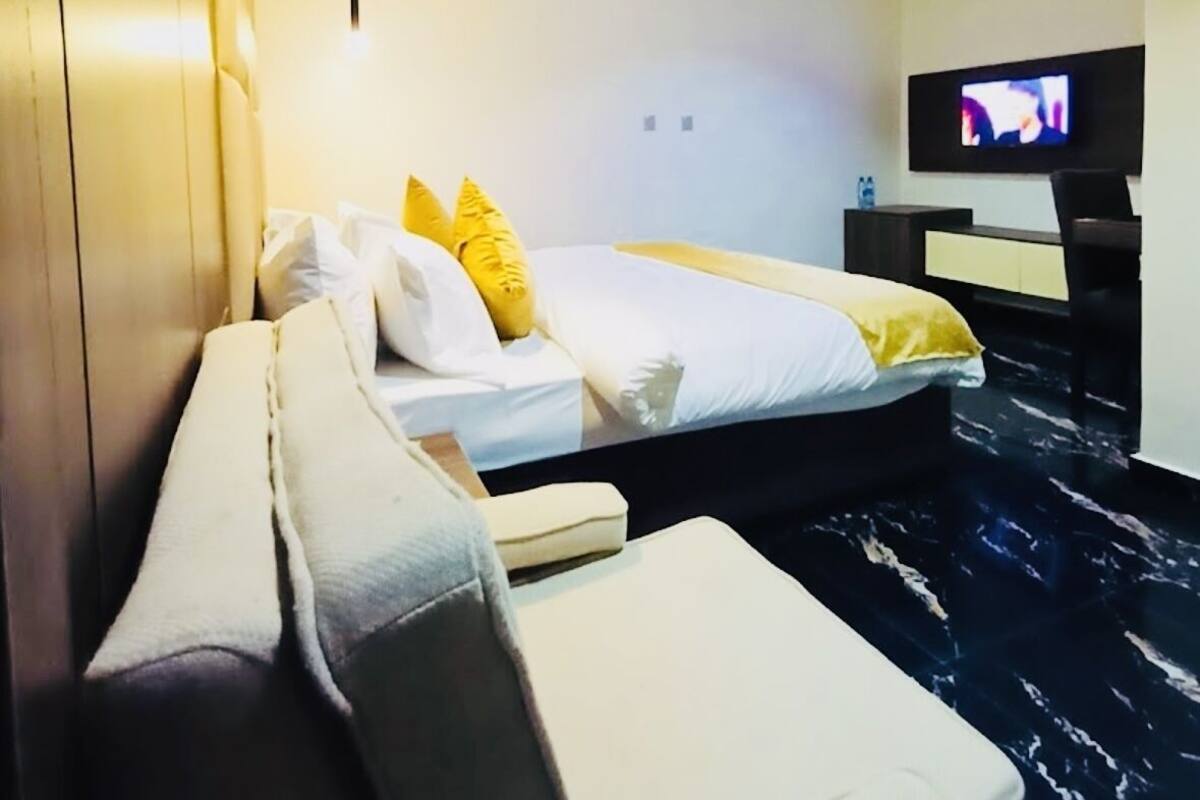 A modern hotel room with a bed, a sofa, a TV, and a marble floor.