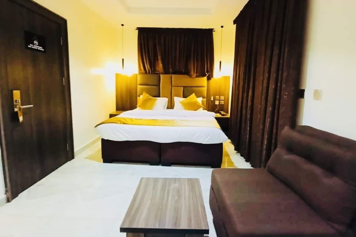 A hotel room with a bed, a sofa, a nightstand, and a lamp.