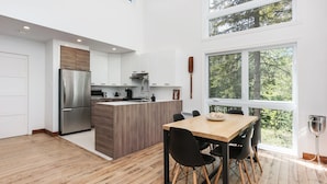 A modern kitchen with a wooden island, stainless steel appliances, and a dining area with black chairs.