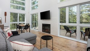 A spacious living room with a fireplace, large windows, and a flat-screen TV.