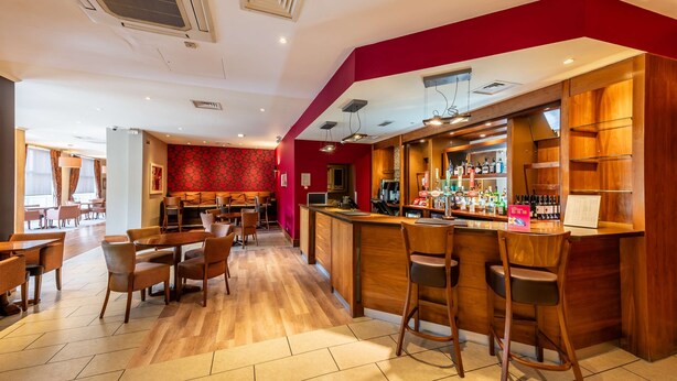 A bar area with wooden furniture, a red accent wall, and a tiled floor. - The Milestone Hotel, Peterborough (Cambridgeshire), Sure Collection by Best Western (Peterborough)