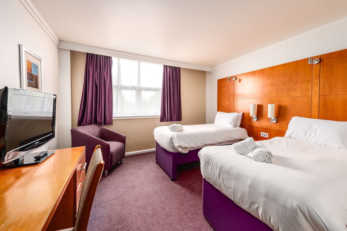 A hotel room with a wooden desk, two beds, a TV, and purple curtains.