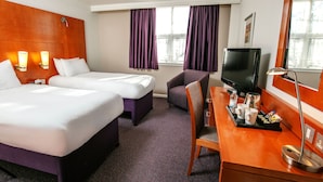 A hotel room with two beds, a desk with a TV, a chair, and a window with curtains. - The Milestone Hotel, Peterborough (Cambridgeshire), Sure Collection by Best Western (Peterborough)