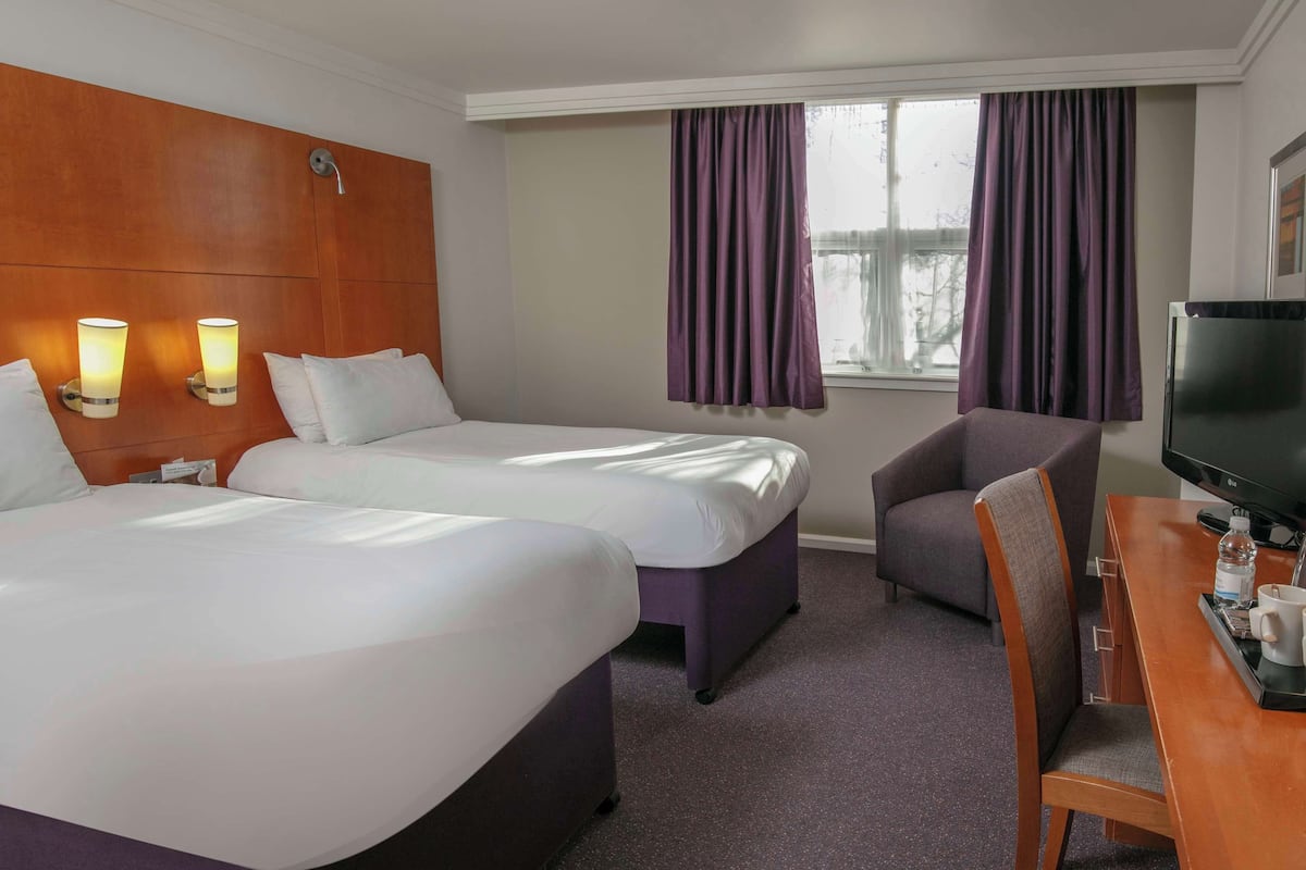 A hotel room with two beds, a desk with a TV, a chair, and a window with curtains.