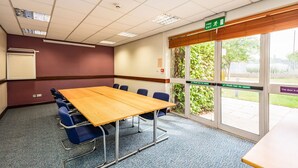 A conference room with a wooden table, blue chairs, a whiteboard, and a window with a view of greenery. - The Milestone Hotel, Peterborough (Cambridgeshire), Sure Collection by Best Western (Peterborough)
