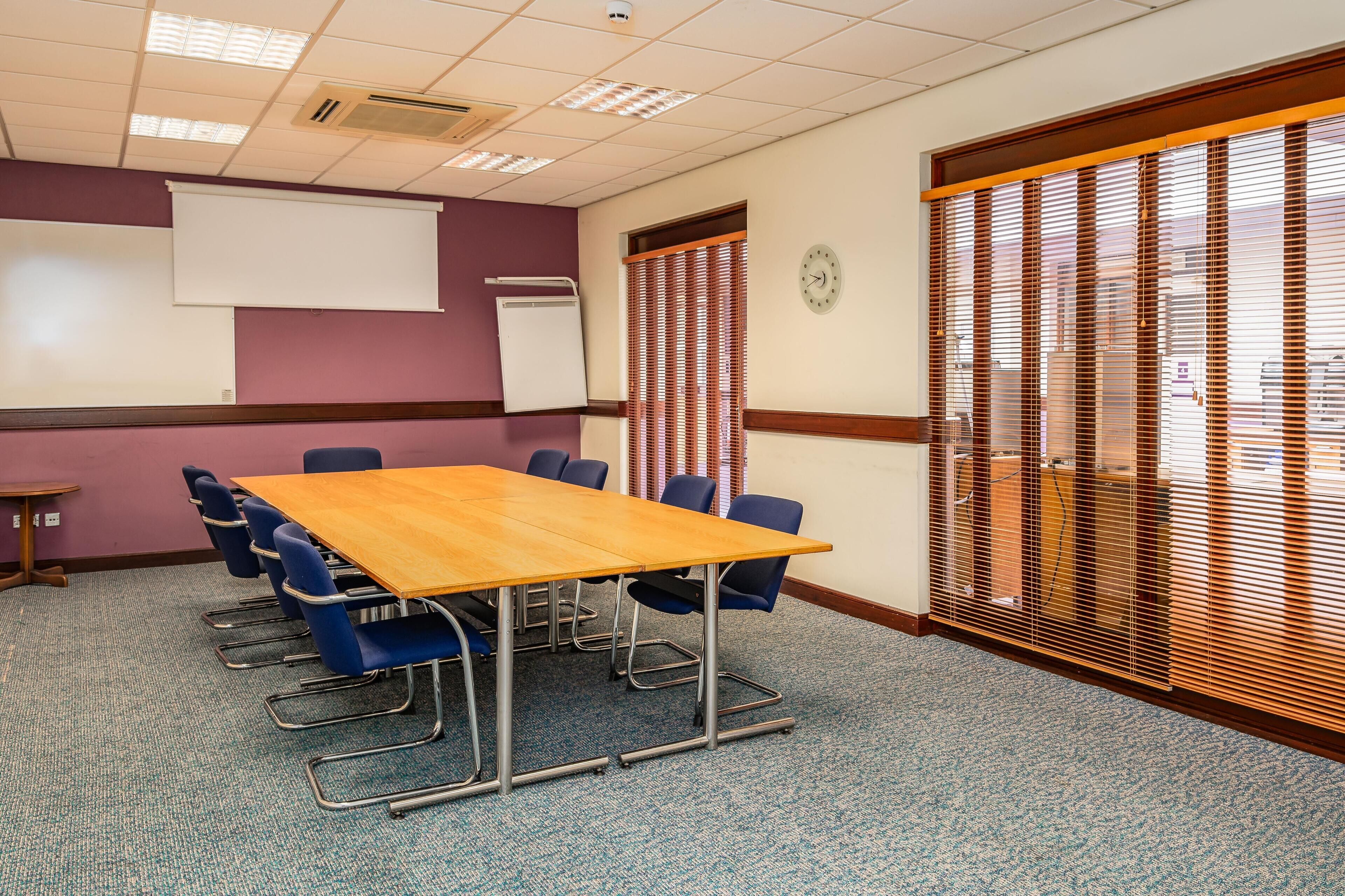 A conference room with a large table, blue chairs, a whiteboard, and a clock on the wall.