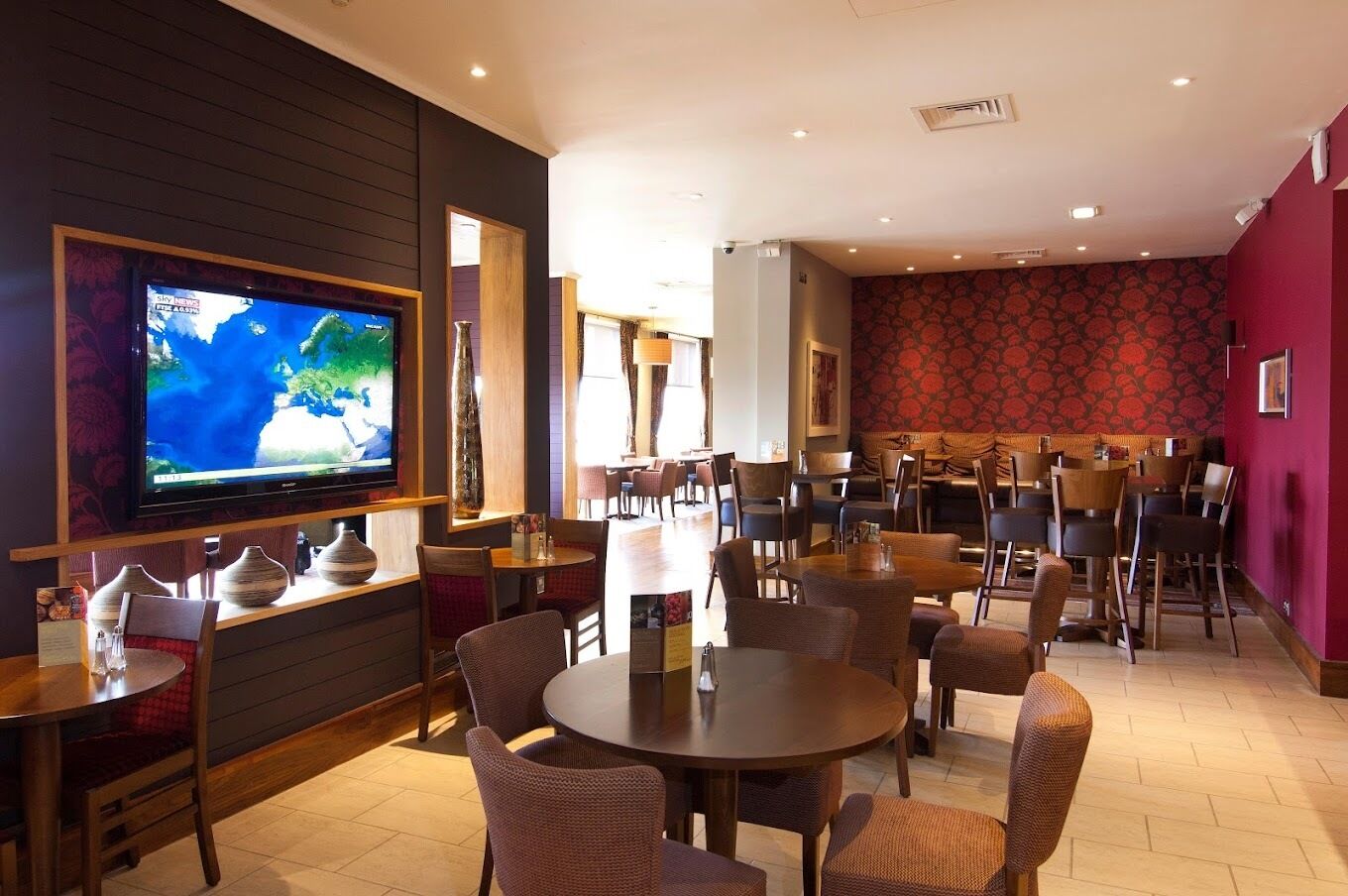 A restaurant with a TV displaying a weather forecast, wooden furniture, and a patterned wall.
