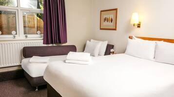 Habitación de hotel con cama, sofá, ventana con cortinas, lámpara de pared e imagen enmarcada.