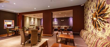 A hotel lobby with multiple seating areas, including a long sofa and several tables and chairs.