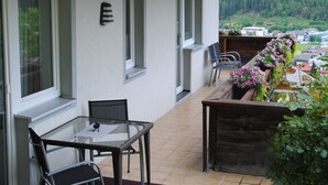 A balcony with a wooden table and chairs, a window, and a view of a forested area. - holiday apartment Elferblick (Fulpmes)