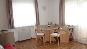 A cozy living room with a wooden floor, a red sofa, a wooden table with two chairs, a bookshelf, and a clock on the wall. - holiday apartment Elferblick (Fulpmes)