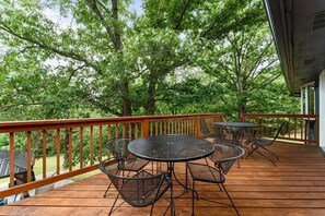 A wooden deck with a round table and chairs, surrounded by trees.