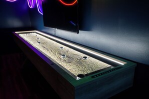A long, narrow, illuminated table with a textured surface and multiple round objects on it, placed against a wall with a flat-screen TV mounted above.