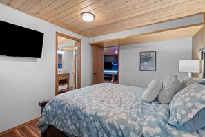 Een slaapkamer met een bed, een televisie, een schilderij en een deur naar een badkamer.