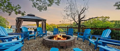 An outdoor seating area with blue Adirondack chairs arranged around a central fire pit.