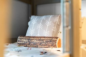 Een stapelbed met een kussen met een bladpatroon en een opgerolde deken.