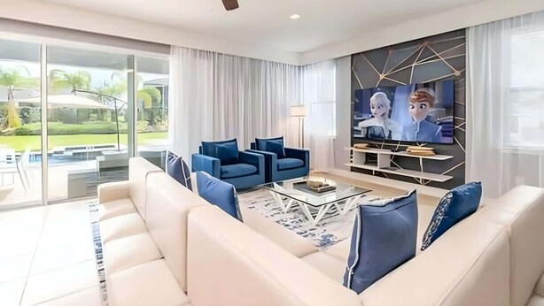 A modern living room with a white sofa, blue armchairs, a coffee table, and a TV mounted on a geometric wall.