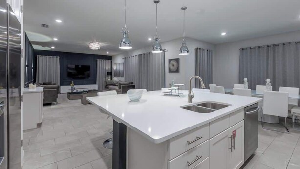 Una cocina moderna con una isla central, armarios blancos e iluminación colgante.