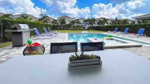 Un área de piscina con sillones reclinables, una parrilla y una mesa con una planta.