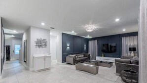 Una sala moderna con un sofá, una mesa de centro y un televisor. Hay una zona de cocina con armarios y una mesa de comedor.