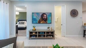 Ein modernes Wohnzimmer mit einem an der Wand montierten Flachbildfernseher, einer grauen Unterhaltungseinheit darunter und einem Durchgang zu einem Schlafzimmer.