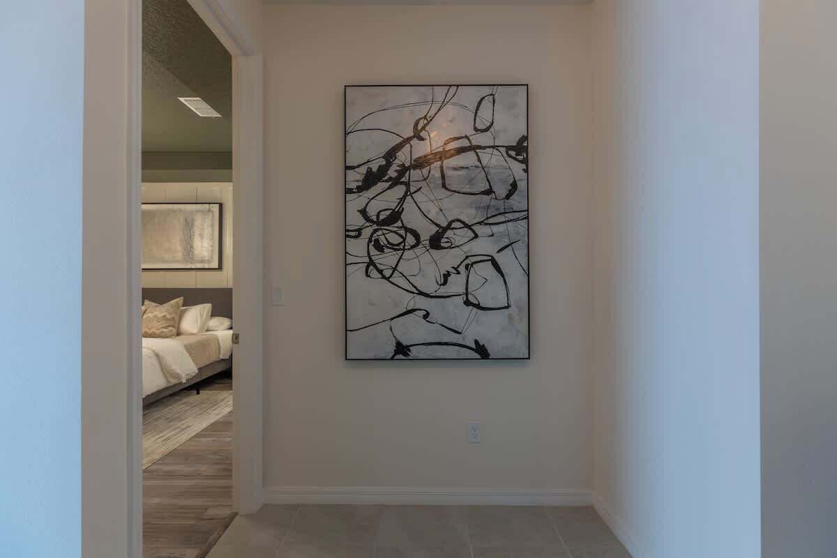 A hallway with a modern abstract painting on the wall, a bed with a neutral color scheme, and a tiled floor.