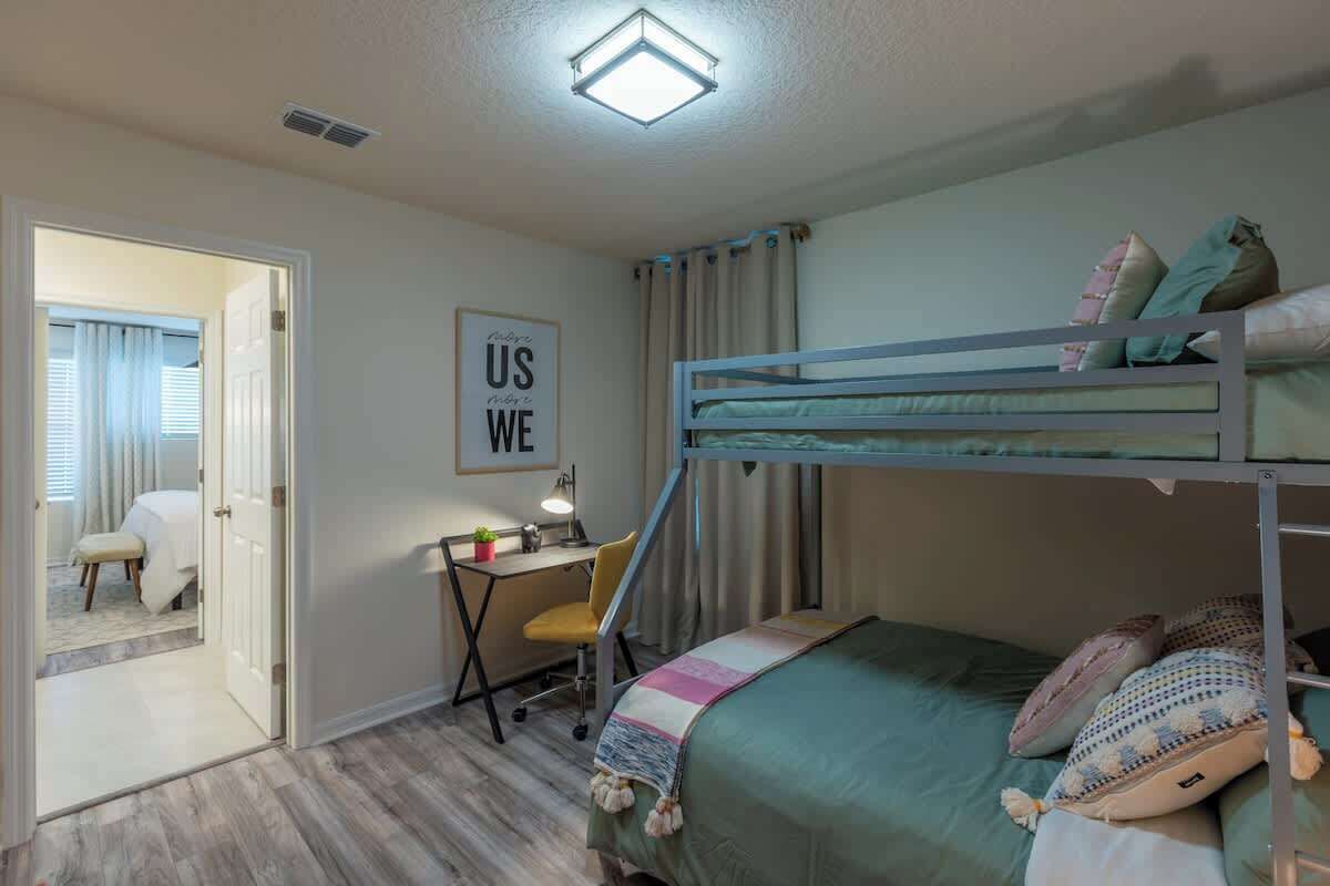 A bunk bed room with a desk and chair, a framed poster, and a door leading to another room.