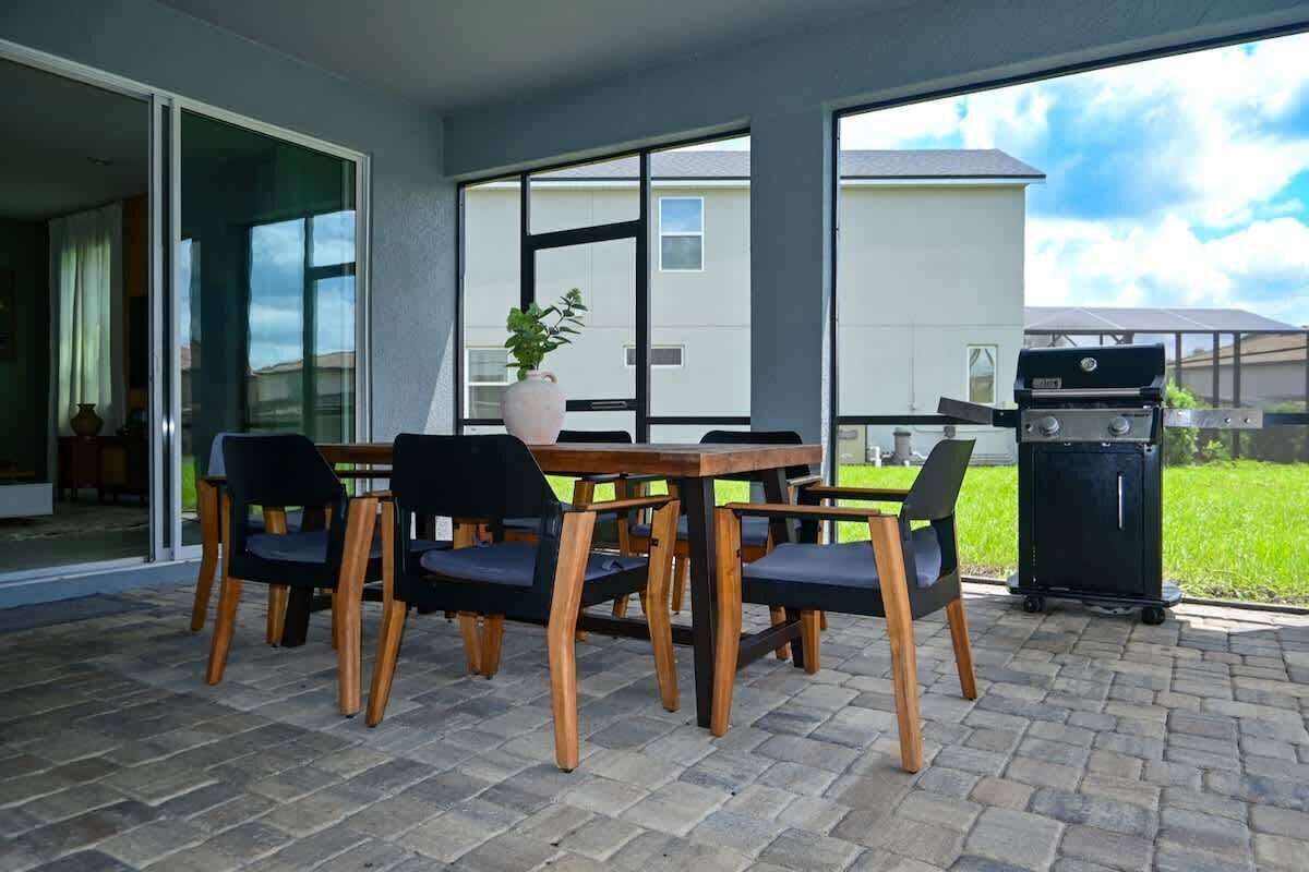 An outdoor patio with a wooden table and chairs, a grill, and a potted plant.
