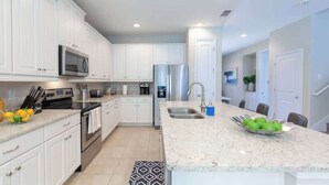 Una cocina moderna con armarios blancos, electrodomésticos de acero inoxidable, una encimera de granito y un tazón de manzanas verdes.