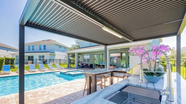 Un área de piscina moderna al aire libre con una parrilla incorporada y asientos.
