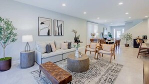 A modern living room with a sofa, coffee table, and chairs. There is a dining area with a table and chairs in the background. - Magical 6BR PetFriendly @Encore Near Disney 7722 (Kissimmee)