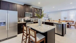 A modern kitchen with dark wood cabinets, stainless steel appliances, and a central island with seating. - Magical 6BR PetFriendly @Encore Near Disney 7722 (Kissimmee)