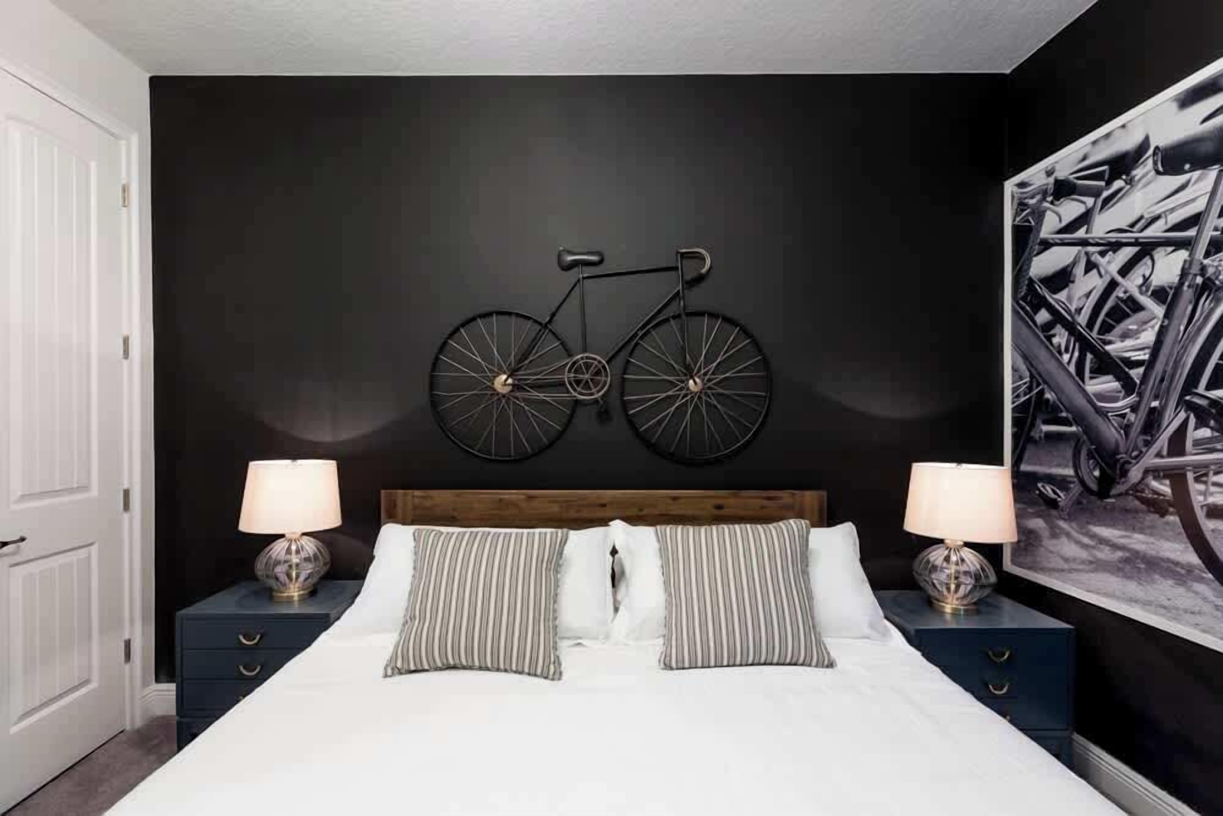 Ein Schlafzimmer mit einem großen Bett, zwei Nachttischen, einem Holzkopfteil, einem Wandbild mit einem Fahrrad und einem gerahmten Bild an der Wand.