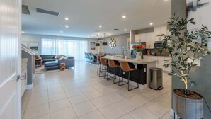 Una cocina moderna con una isla central, taburetes de bar y un comedor con sofá y sillas.