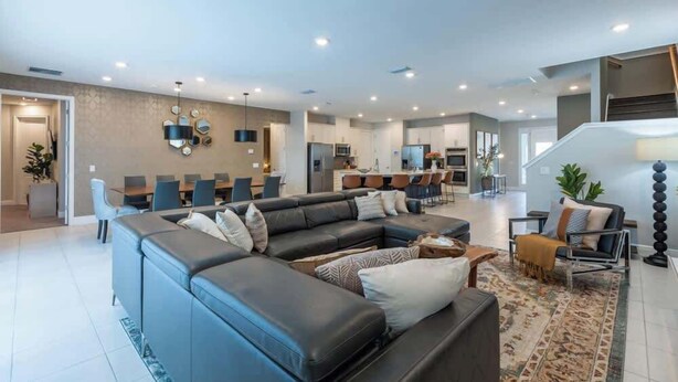 Una sala moderna con sofá seccional, comedor, cocina y escalera.