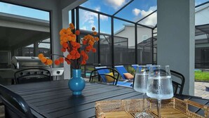 An outdoor dining area with a table, chairs, a grill, and a vase of flowers.